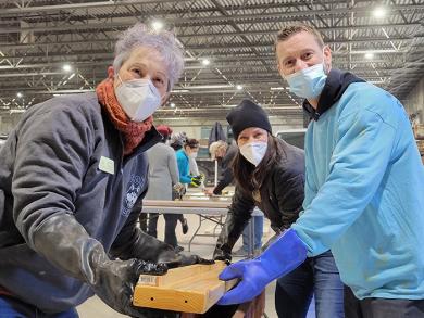 From left, Jackie Riffice, Stephanie Wright and Dave King pull a side rail from a stain solution during the Build-a-Bed event Jan. 16. (EC)